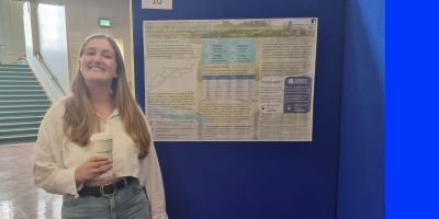 Katie Lewis, smiling, standing next to a poster titled