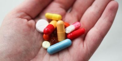 Close up of a hand with a handful of pills of different colours, shapes and sizes
