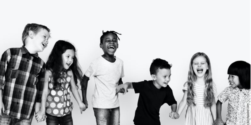 black and white image of six primary school children holding hands and laughing