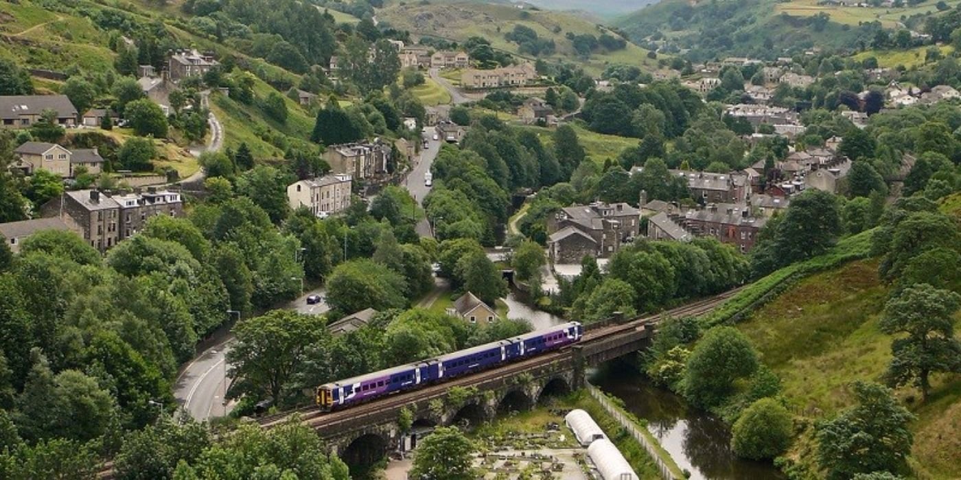 Small local train crossing a river and a road through a rural, hilly village.