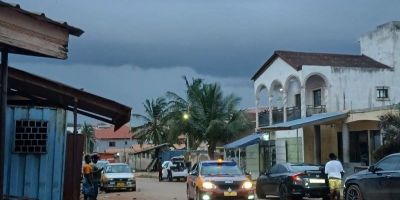A street in Ghana with cars driving through it and dark storm clouds above.