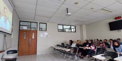 A class of students in Indonesia watching a lecture by Professor Jon Lovett, who's on a screen at the front of the classroom