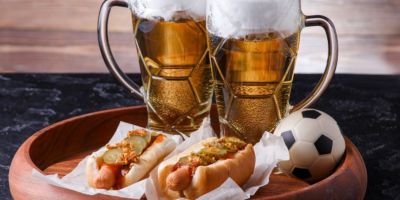 A tray with two classes of beer, two hot dogs and a mini football.