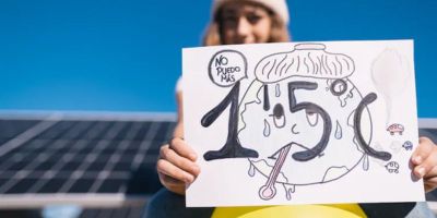 Climate protestor holding up a square white sign about the 1.5 degree celsius global warming limit goal.