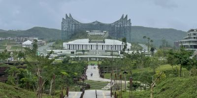 A large, modern palace at the end of a long, winding path through rich green land