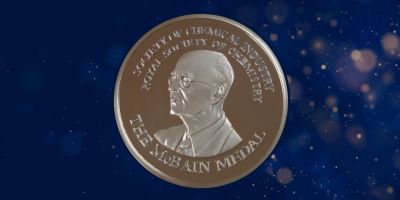 A golden coin on a dark blue background. The coin has James William McBain in the middle and says 