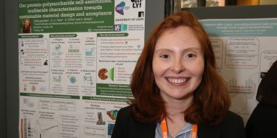 Jennifer McLauchlan smiling to the camera, in front of her poster describing research with Oatly about microgels