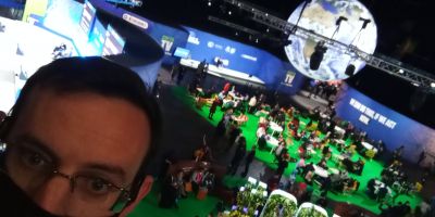 Man stands abover large conference with glowing globe suspended from ceiling and letters COP26 in leaves