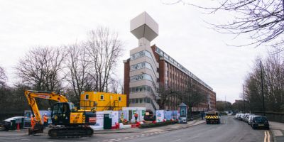 Image showing University of Leeds building with a drilling site in front. A digger and the Leeds Climate Plan banner are in front.
