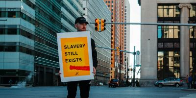 A person stood in the street in front of a high rise building, holding a sign that says 