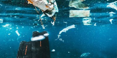 A person's feet in flippers underwater, swimming amongst plastic bags and smaller pieces of plastic.