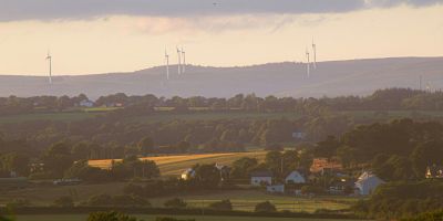 Rural England with houses dotted between fields and wind turbines on the horizon