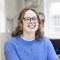 Lauren is a white woman with shoulder length brown hair and glasses. She is smiling and wearing a blue jumper.