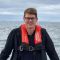 Edward Whittle standing on a boat, with the sea in the background.