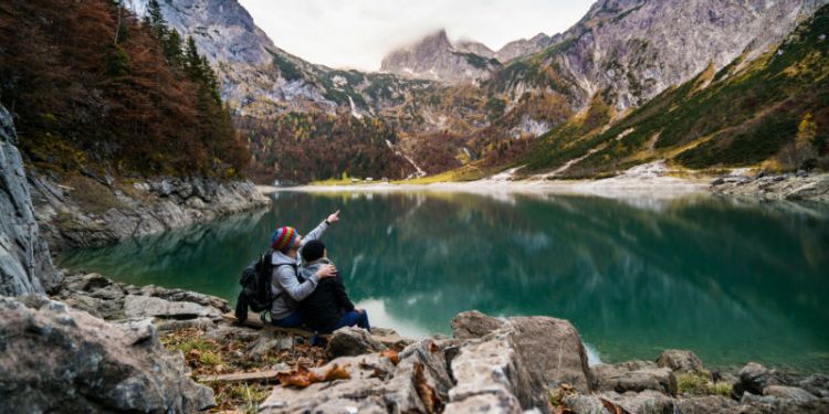 Two people sit on rocks with a view over a lake with mountains in the distance