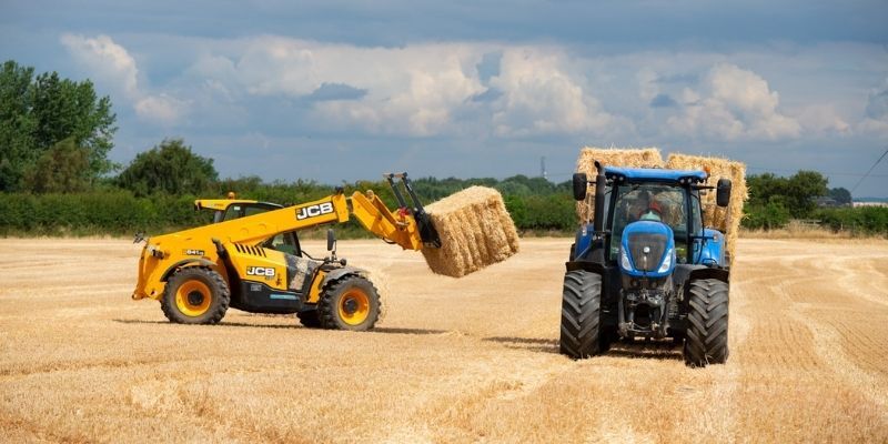 A hay baler loading a bale of hay on to a tractor, in a field.